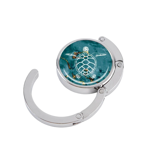 NOOX Laguna foldable metal bag hanger featuring a white sea turtle design on a deep turquoise marble background